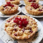 Leckere Johannisbeer-Tartelettes mit Streuseln und Vanillepudding auf einem Teller