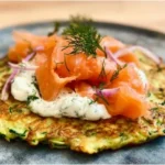 Zucchini-Pfannkuchen mit Räucherlachs auf einem Teller garniert
