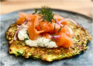 Zucchini-Pfannkuchen mit Räucherlachs auf einem Teller garniert
